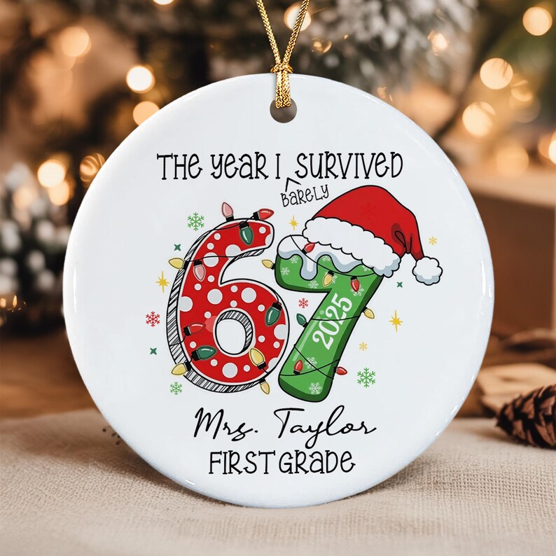 A round white ceramic ornament featuring the text "THE YEAR I SURVIVED BARELY" above a large red polka-dot number 6 and a green number 7 wearing a Santa hat. The number 7 includes "2025". Below are "Mrs. Taylor" and "FIRST GRADE".