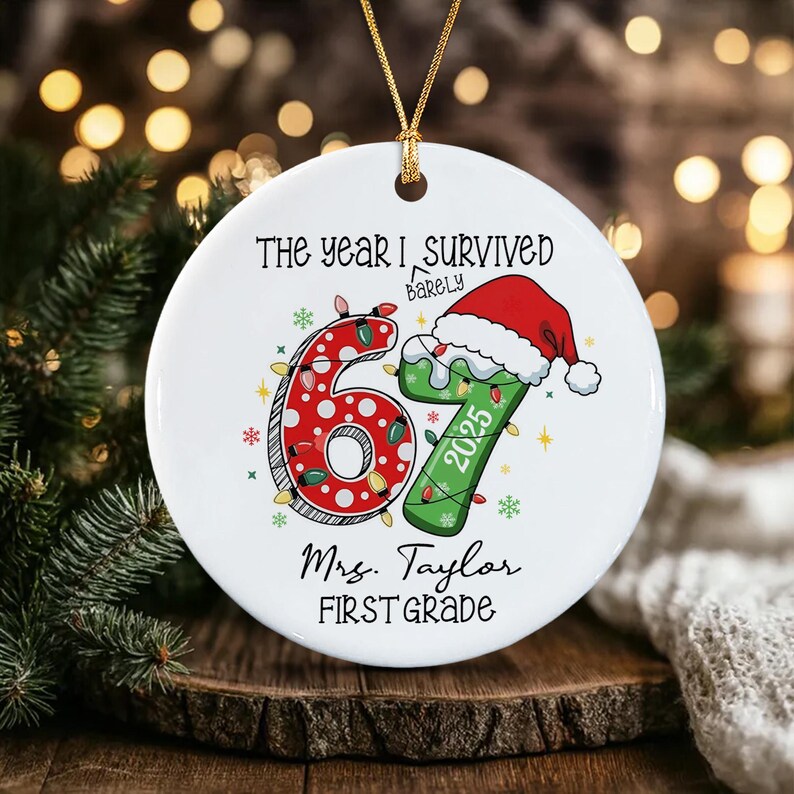 A round white ceramic ornament with a gold string. The design features the text THE YEAR I SURVIVED BARELY, the number 67 with red polka dots and green colors, a Santa hat, the year 2025, and the text Mrs. Taylor FIRST GRADE.