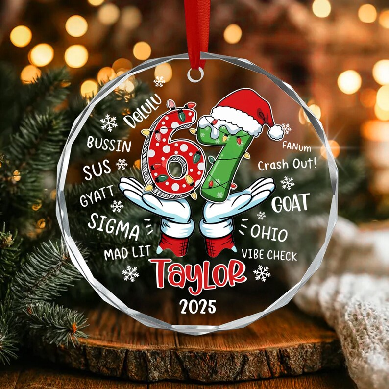 A circular clear acrylic ornament featuring the number 67 in red and green with a Santa hat, held by cartoon gloved hands.