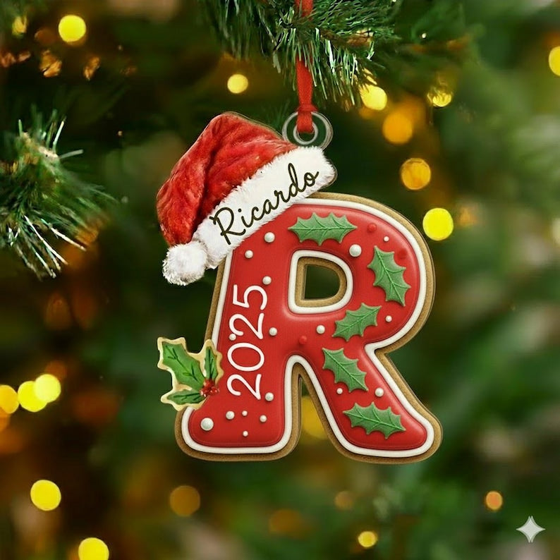 A red letter R Christmas ornament shaped like a gingerbread cookie with white icing dots and green holly leaves. A red Santa hat sits on top with the name Ricardo written in black script and the year 2025 printed in white text.