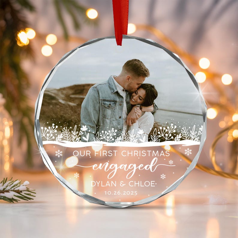A round, faceted glass ornament featuring a photo of a couple embracing outdoors. The text reads: OUR FIRST CHRISTMAS engaged DYLAN & CHLOE 10.26.2025.