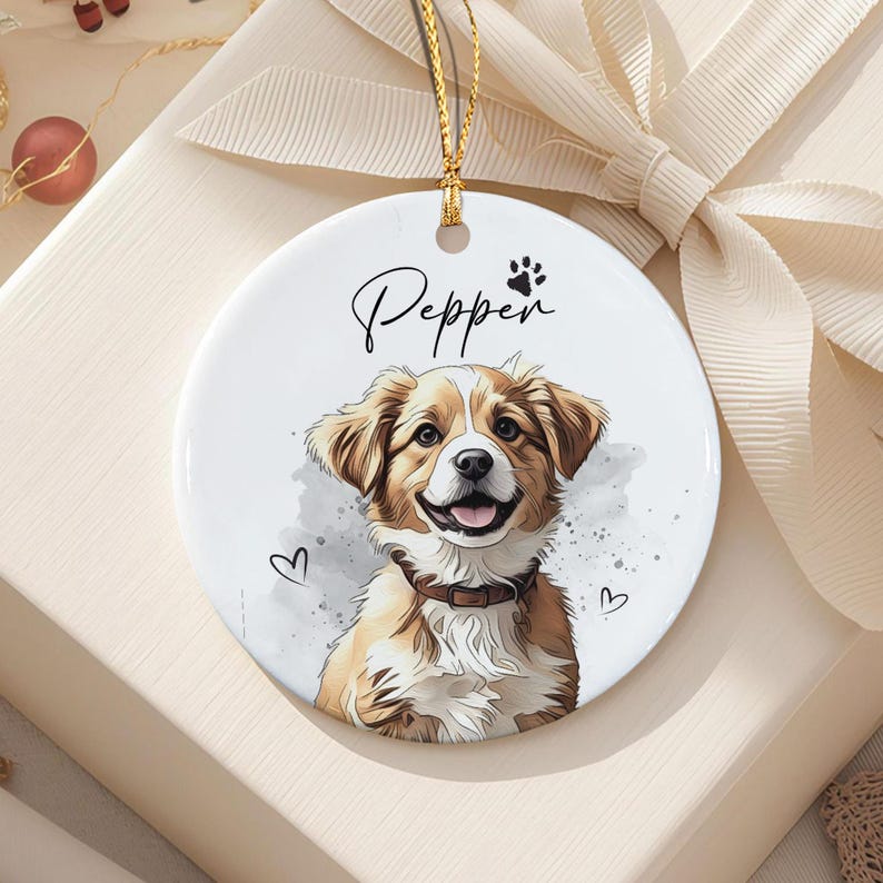 A round white ceramic ornament featuring a colorful illustration of a brown and white dog with a dark collar. The name Pepper is printed in black script above the dog, accompanied by a small paw print and two outlined hearts.