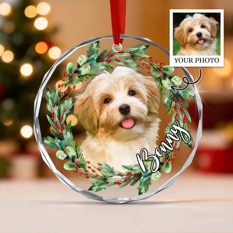 A circular, faceted glass ornament featuring a custom portrait of a light-colored puppy with a pink tongue. The puppy is framed by a wreath of green leaves and red berries.