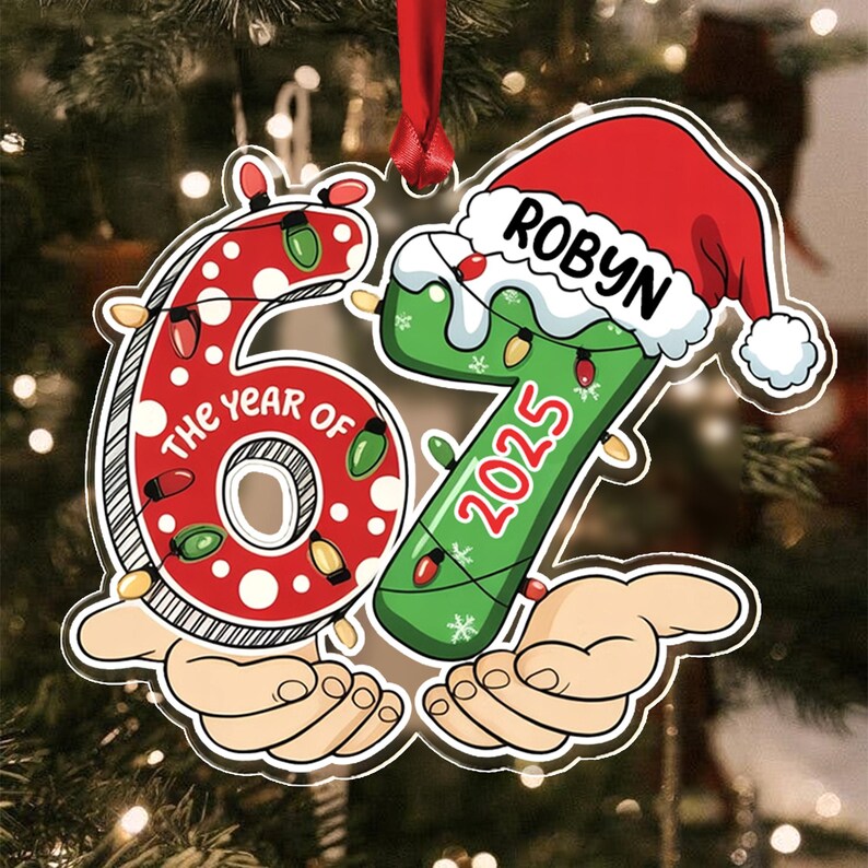A flat Christmas ornament shaped like the number 67, featuring a red polka-dot 6 and a green 7 with a Santa hat. The text reads THE YEAR OF, ROBYN, and 2025.