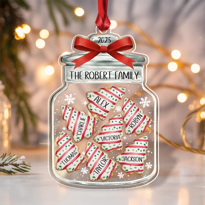 A clear, jar-shaped Christmas ornament featuring a red ribbon bow at the top and the text 2025. The jar is labeled THE ROBERT FAMILY and contains six tree-shaped cookies with red and green stripes, each personalized with names.