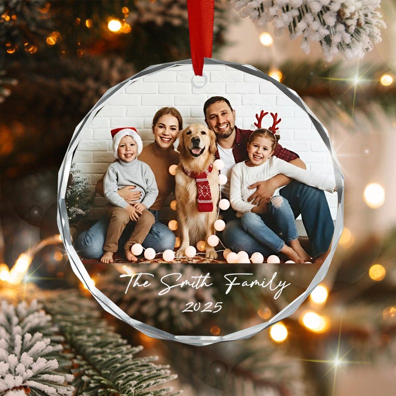 A circular, faceted glass Christmas ornament featuring a printed photograph of a family with a dog. The image shows two adults, two children, and a golden retriever wearing a red scarf. The text reads The Smith Family 2025.