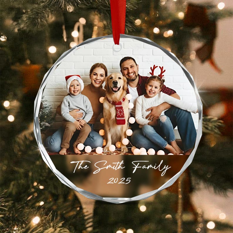 A circular glass Christmas ornament featuring a printed family photograph of two adults, two children, and a golden retriever. The text "The Smith Family" and "2025" is printed in white script below the photo.