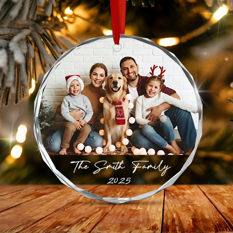 A circular glass Christmas ornament featuring a printed family photograph of two adults, two children, and a golden retriever dog. The text "The Smith Family 2025" is printed in white script at the bottom.