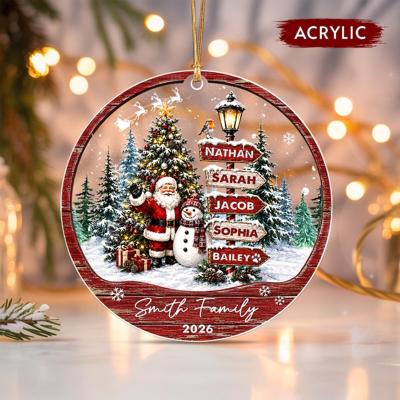 A round acrylic Christmas ornament featuring a winter scene with Santa Claus, a snowman, a decorated tree, and a street sign post with the names Nathan, Sarah, Jacob, Sophia, and Bailey.