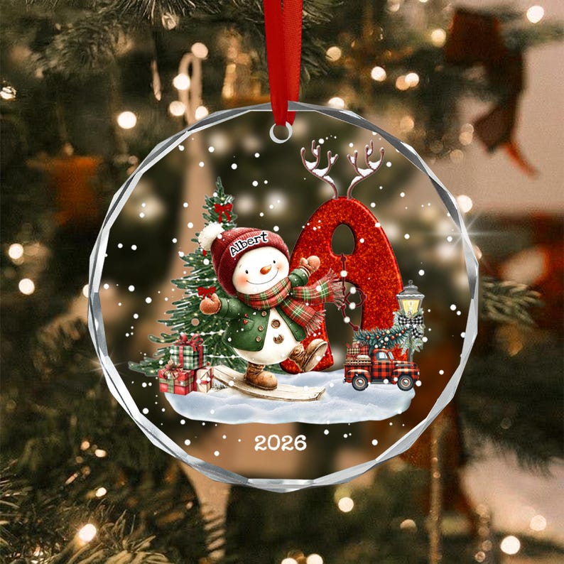 A circular glass Christmas ornament featuring a snowman wearing a red hat with the name Albert, a green coat, and a plaid scarf.