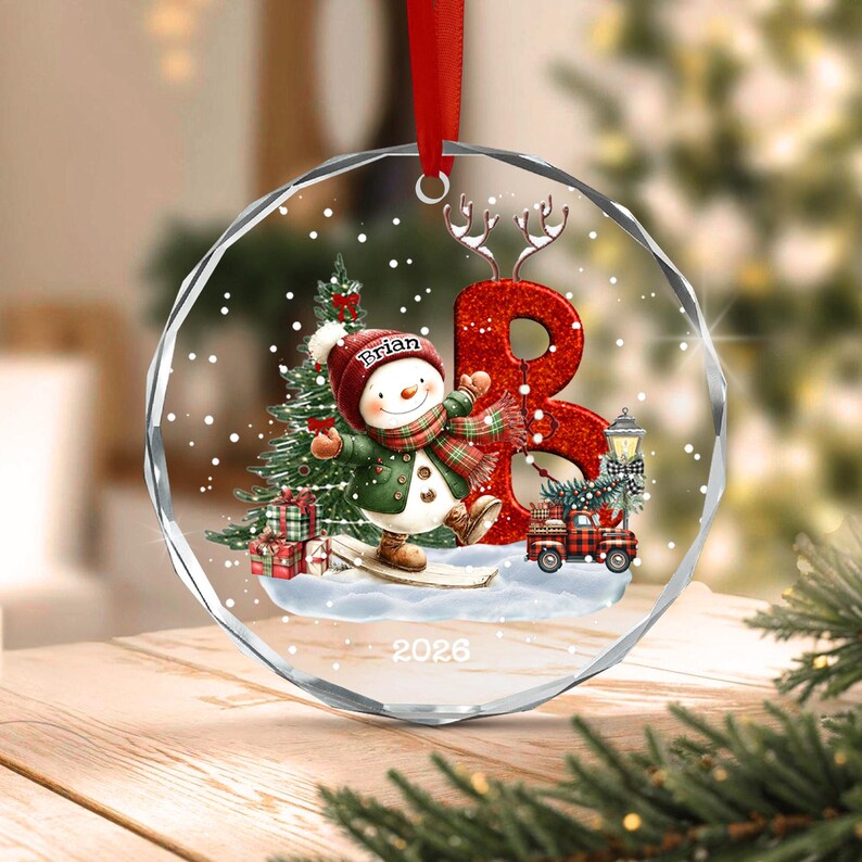 A circular glass Christmas ornament featuring a snowman wearing a red hat with the name Brian, a green coat, and a plaid scarf.