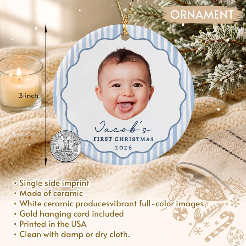 A round ceramic ornament featuring a light blue and white striped border with a scalloped edge. The center displays a photograph of a baby, the text Jacob's FIRST CHRISTMAS 2026, and a gold hanging cord.