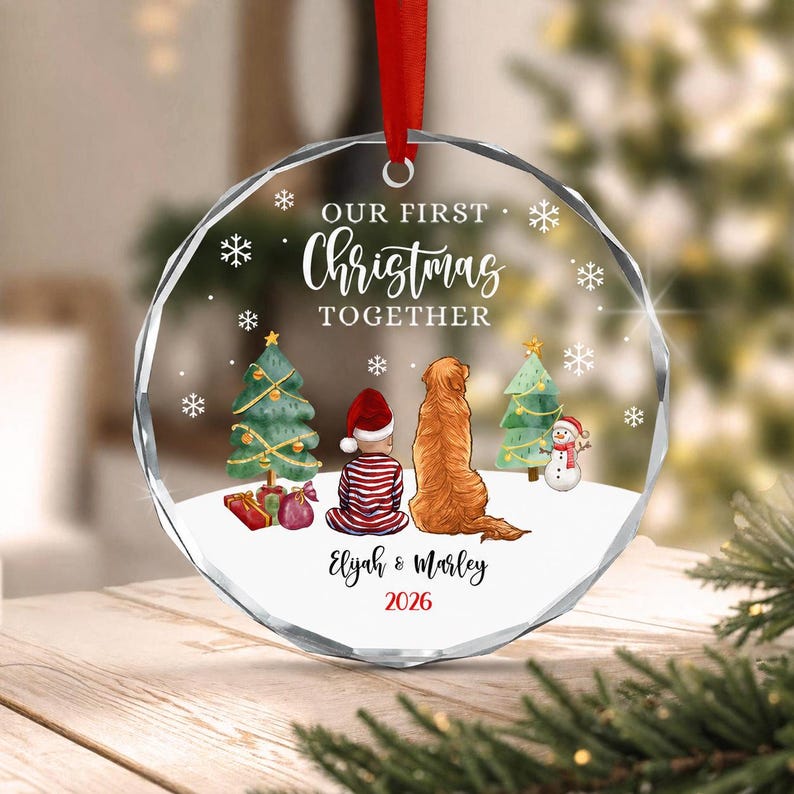 A circular clear glass Christmas ornament with a red ribbon hanger.