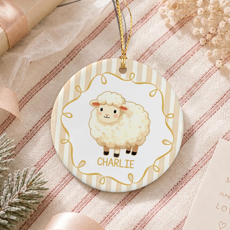A round ceramic ornament featuring a white fluffy sheep illustration centered within a gold swirling frame. The background has vertical beige and white stripes. The name CHARLIE is printed in gold below the sheep.