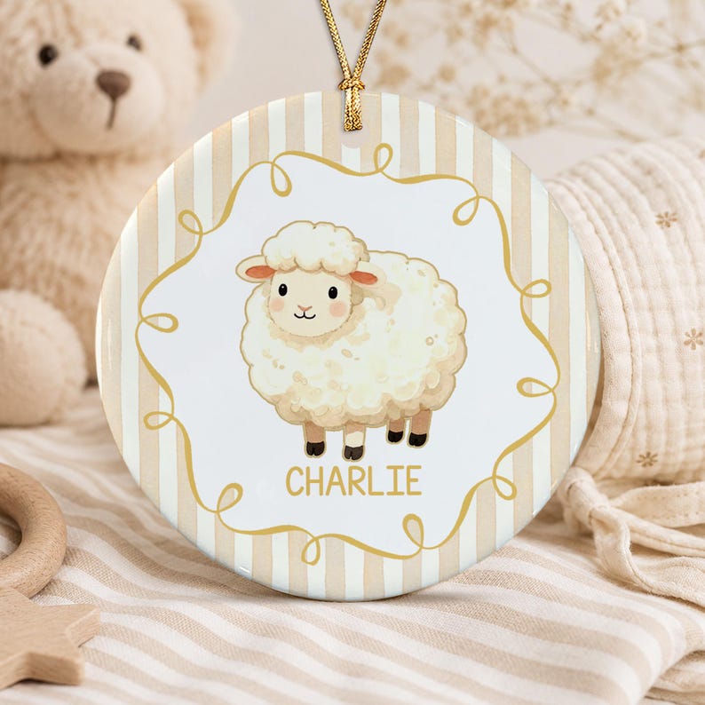 A round ceramic ornament featuring a white fluffy sheep illustration centered within a gold swirling frame. The background has vertical beige and white stripes. The name CHARLIE is printed in gold below the sheep.