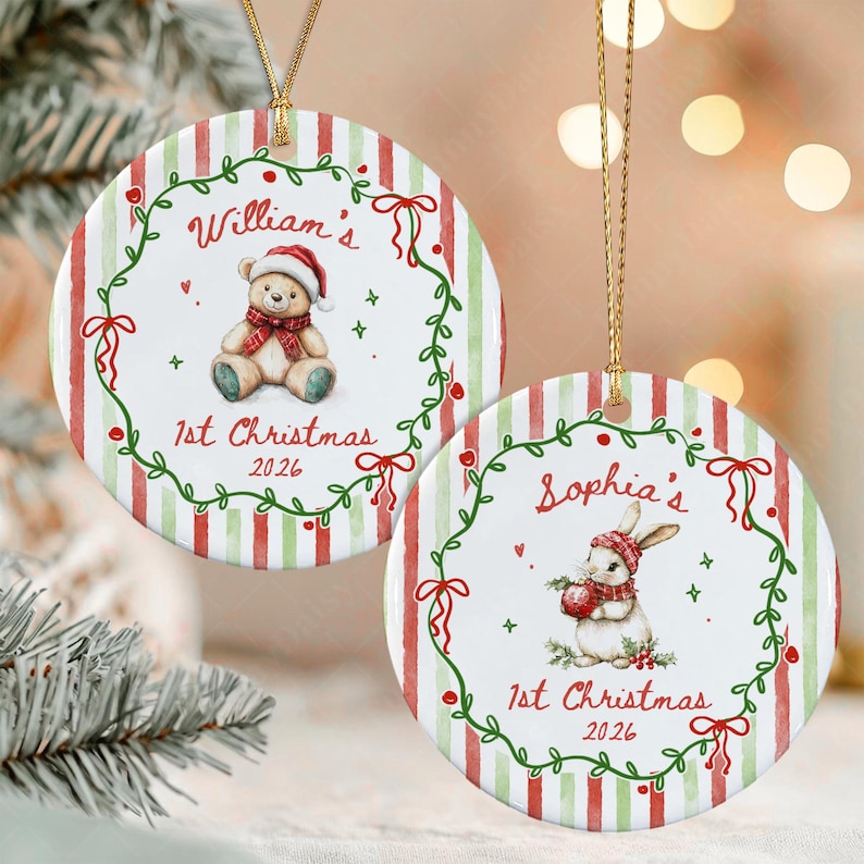 Two round ceramic ornaments with gold hanging strings. One features a teddy bear in a Santa hat with the text William's 1st Christmas 2026. The other shows a rabbit in a winter hat with the text Sophia's 1st Christmas 2026.