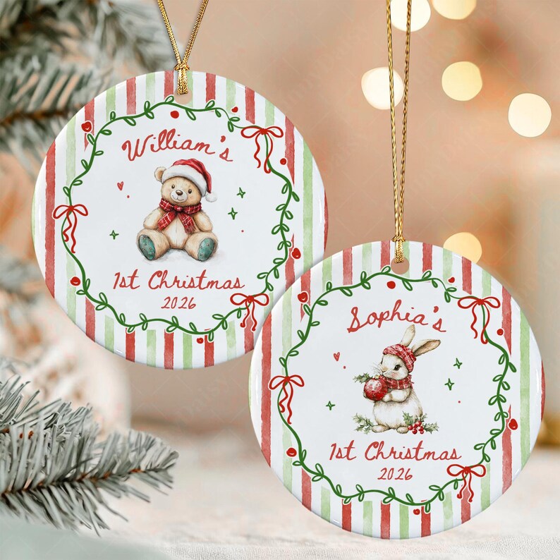 Two round ceramic ornaments with gold hanging strings. One features a teddy bear in a Santa hat with the text William's 1st Christmas 2026. The other shows a rabbit in a winter hat with the text Sophia's 1st Christmas 2026.