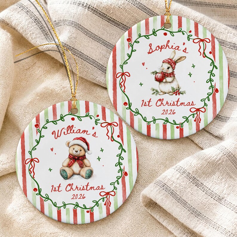 Two round ceramic Christmas ornaments with gold hanging strings. One features a teddy bear in a Santa hat with the text "William's 1st Christmas 2026". The other shows a rabbit in a winter hat with "Sophia's 1st Christmas 2026".