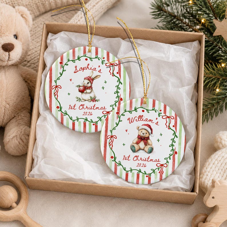 Two round ceramic ornaments with gold hanging strings. One features a rabbit in a red hat with the text Sophia's 1st Christmas 2026. The other features a teddy bear in a red hat with the text William's 1st Christmas 2026.