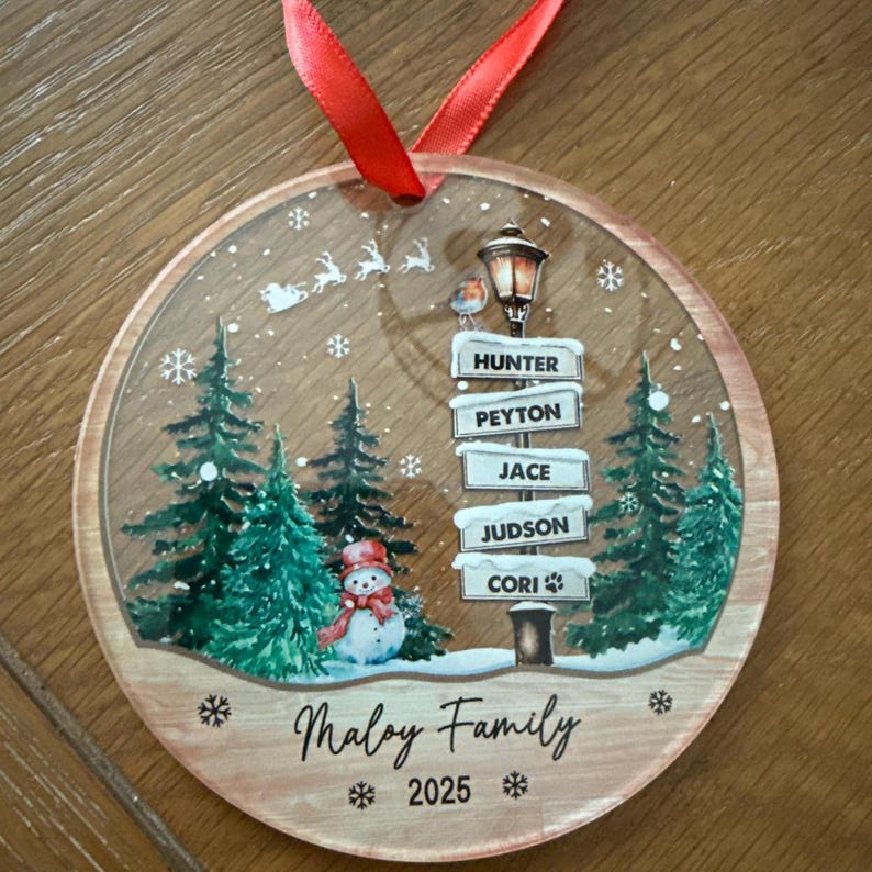 A round, clear acrylic Christmas ornament with a red ribbon hanger.