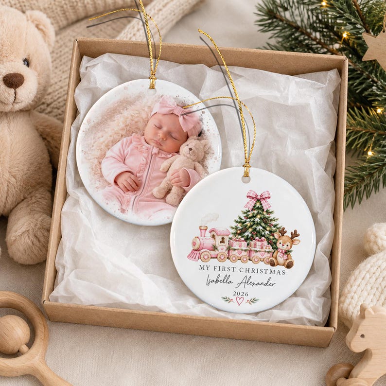 Two round white ceramic ornaments with gold hanging strings. One features a photograph of a baby in pink clothing holding a teddy bear.