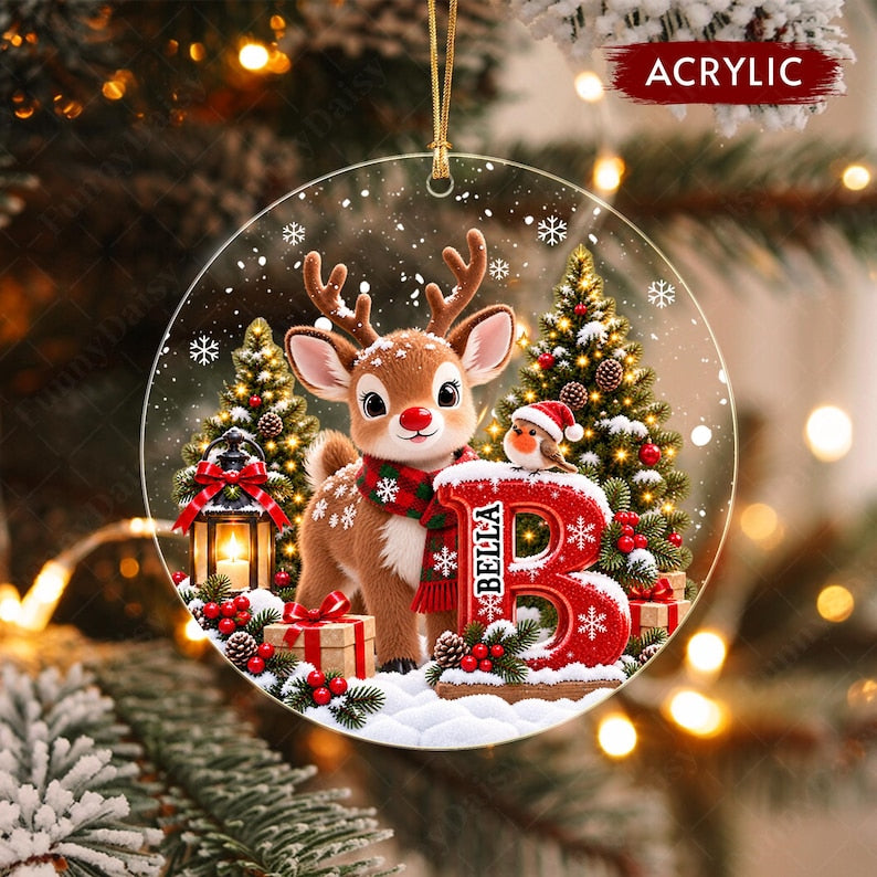 A round acrylic Christmas ornament featuring a brown reindeer wearing a red and green plaid scarf, standing next to a large red letter B with the name BELLA printed on it.