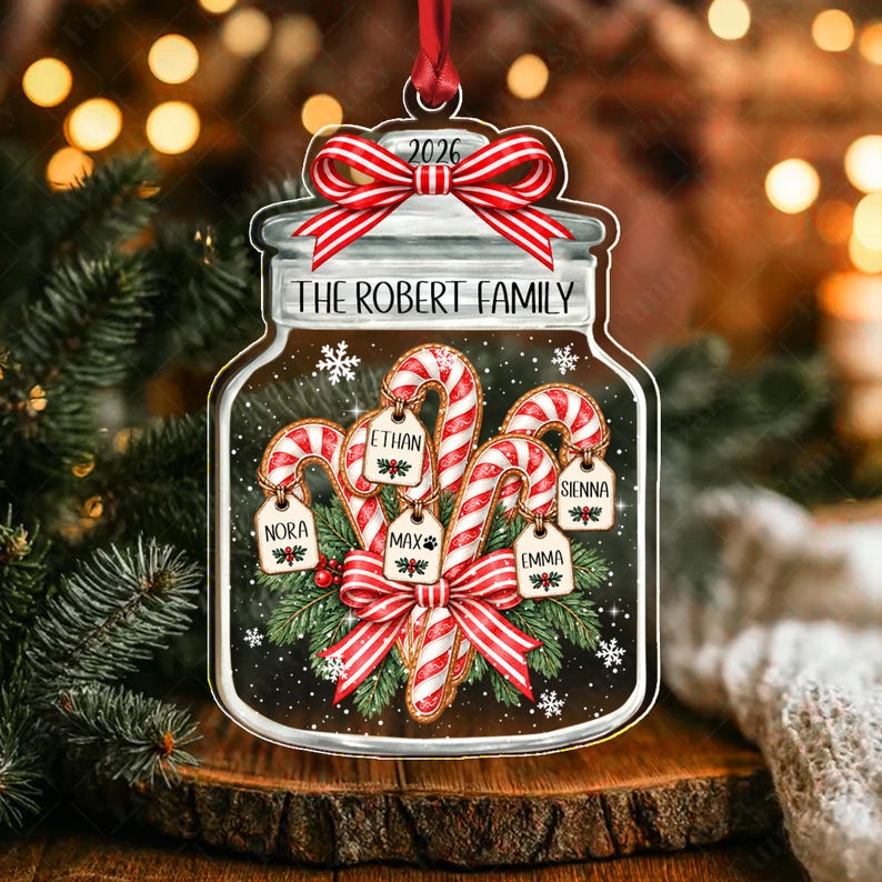 A flat, jar-shaped Christmas ornament featuring a red and white striped bow at the top with the year 2026. The text reads THE ROBERT FAMILY. Inside the jar are candy canes with tags labeled NORA, ETHAN, MAX, SIENNA, and EMMA.