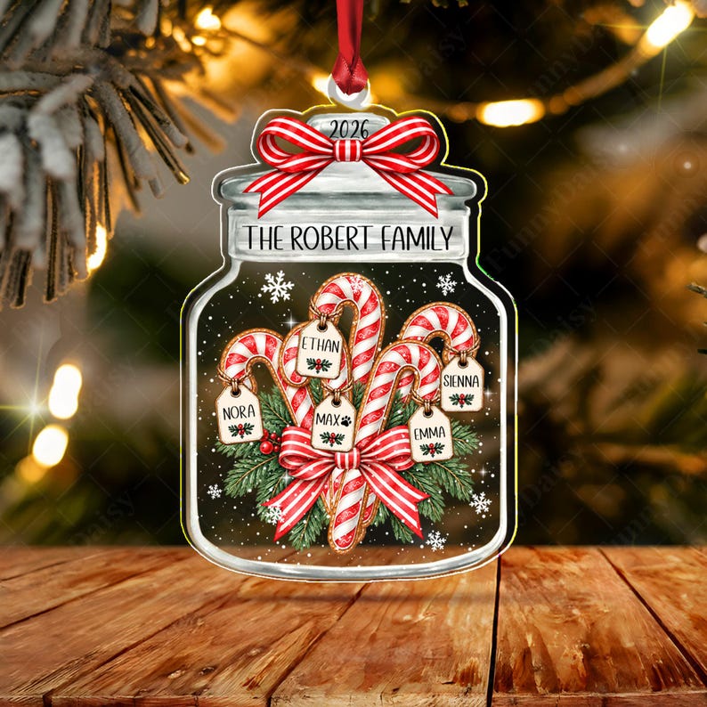 A flat, jar-shaped Christmas ornament featuring a red and white striped bow at the top with the year 2026. The jar is labeled THE ROBERT FAMILY and contains candy canes with tags labeled NORA, ETHAN, MAX, SIENNA, and EMMA.