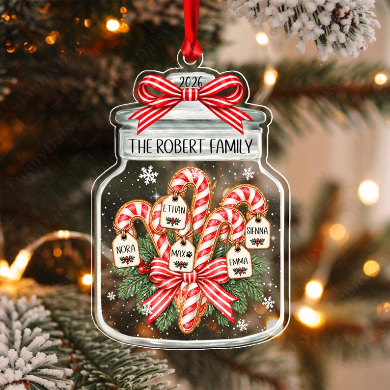 A clear, jar-shaped Christmas ornament featuring a red and white striped bow at the top with the year 2026. The text THE ROBERT FAMILY is printed below. Inside are candy canes with tags labeled Nora, Ethan, Max, Sienna, and Emma.