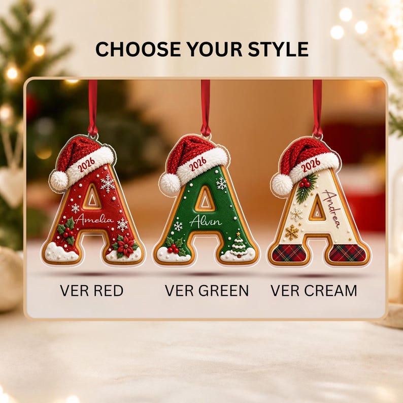Three letter A-shaped Christmas ornaments with red Santa hats and the year 2026. The first is red with white snowflakes and holly, the second is green with white snowflakes and a tree, and the third is cream with plaid accents.
