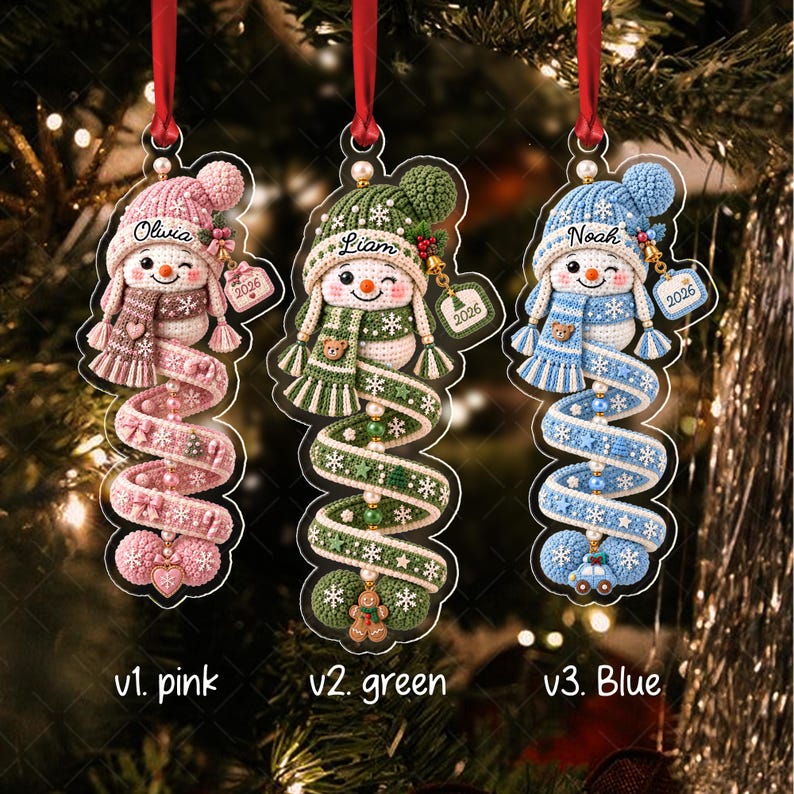 Three hanging ornaments featuring crocheted-style snowmen in pink, green, and blue. Each snowman wears a matching hat and scarf, with a spiral tail decorated with beads and small charms.