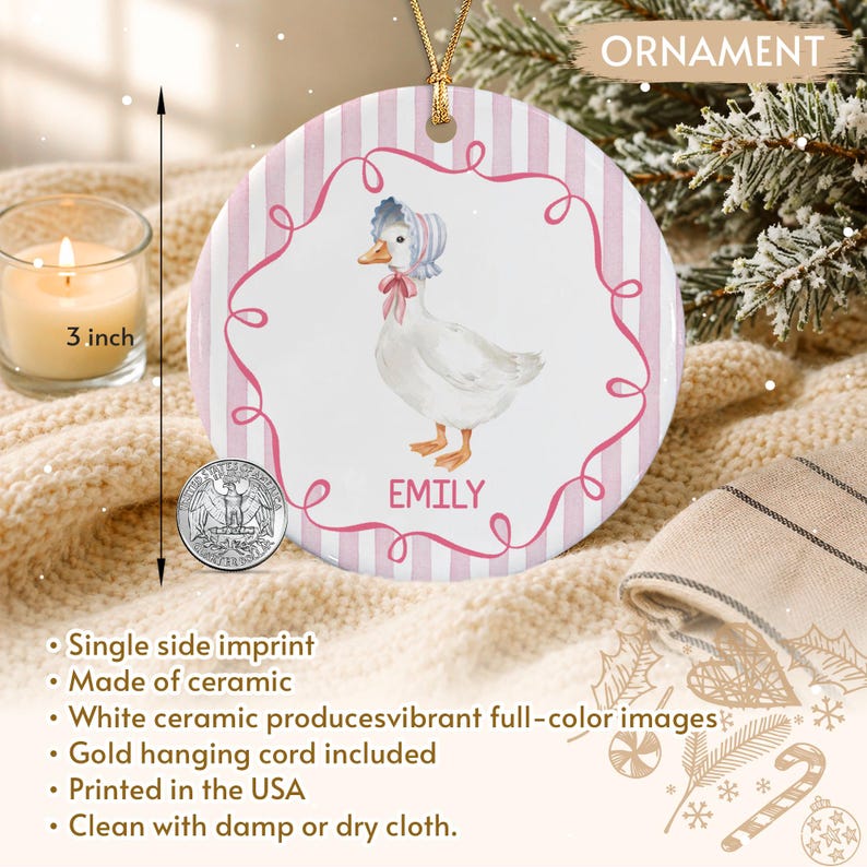 A round white ceramic ornament featuring a pink and white striped background with a central illustration of a white duck wearing a bonnet and pink bow. The name EMILY is printed in pink below the duck, and a gold cord is attached.