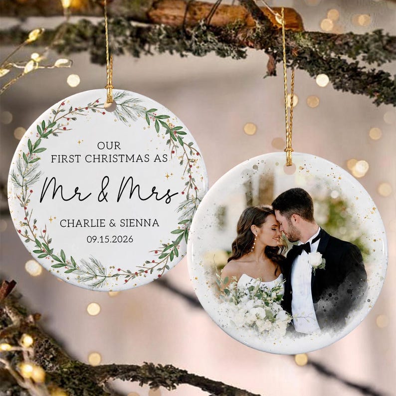 Two round ceramic ornaments hanging by gold strings. One features a green pine wreath design with the text "OUR FIRST CHRISTMAS AS Mr & Mrs CHARLIE & SIENNA 09.15.2026".