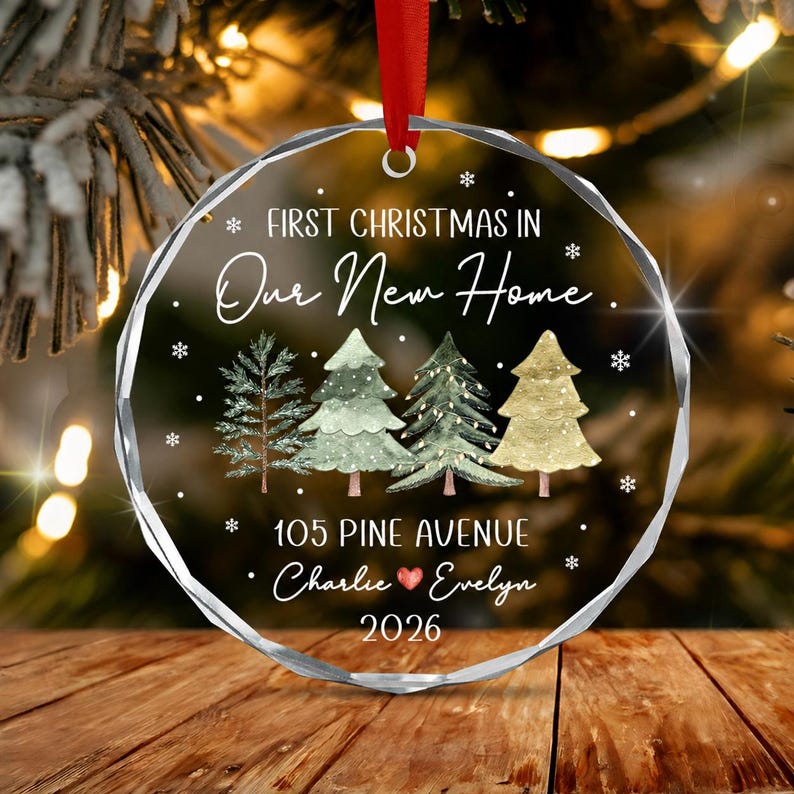 A circular clear acrylic Christmas ornament with a faceted edge, featuring the text "FIRST CHRISTMAS IN Our New Home", "105 PINE AVENUE", "Charlie ♥ Evelyn".