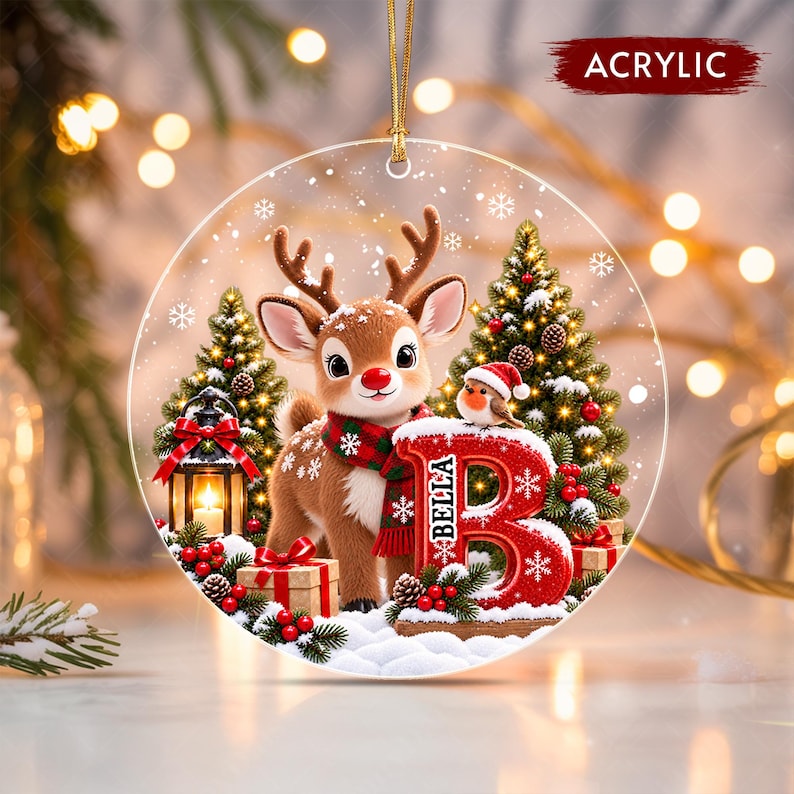 A round acrylic Christmas ornament featuring a cartoon reindeer wearing a red and green plaid scarf, standing next to a large red letter B with the name BELLA printed on it.