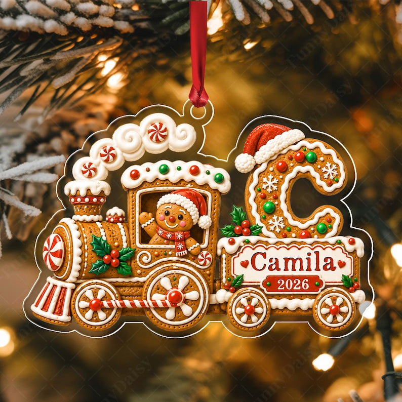 A gingerbread train Christmas ornament featuring a gingerbread person in a Santa hat, a large letter C decorated with snowflakes, and a banner with the text Camila 2026.