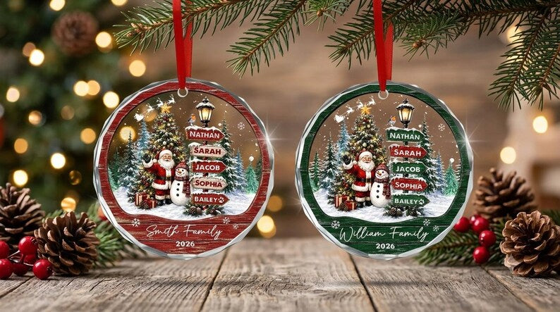 Two round, faceted glass Christmas ornaments with red ribbons. Each features a winter scene with Santa, a snowman, a Christmas tree, and a street sign listing names.