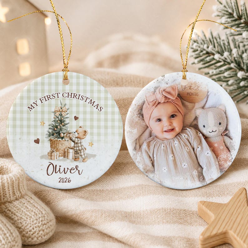 Two round ceramic ornaments with gold hanging strings. One features a green gingham background, a teddy bear, a Christmas tree, and the text "MY FIRST CHRISTMAS Oliver 2026".