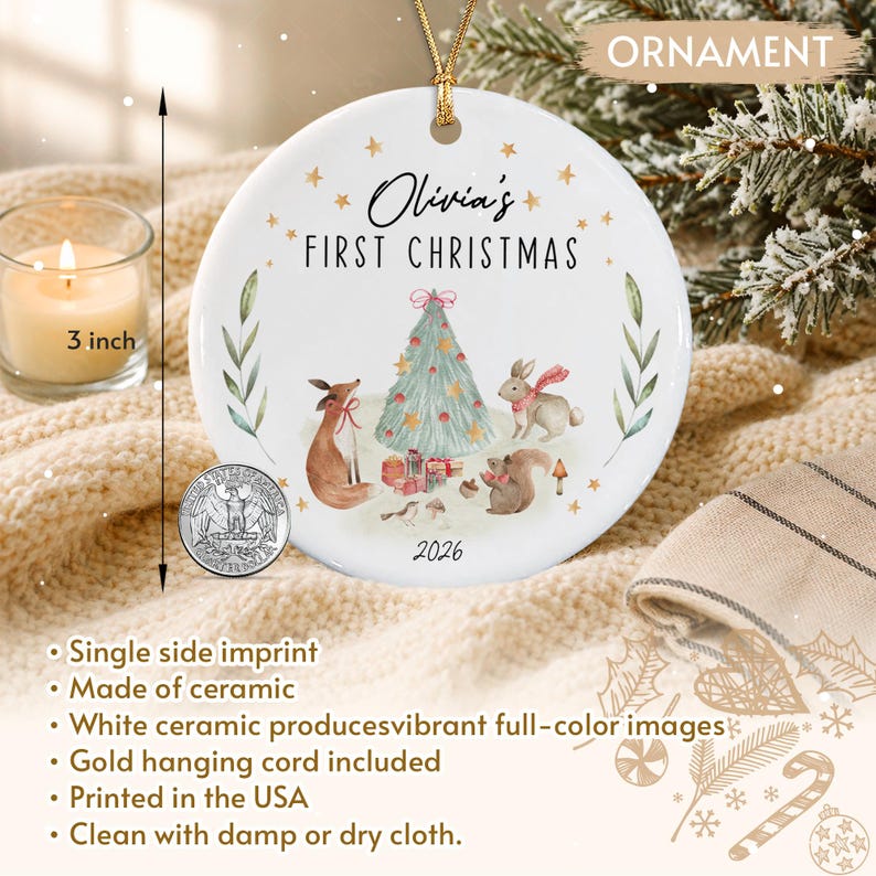 A round white ceramic ornament featuring a gold hanging cord and a 3-inch diameter. The design includes a Christmas tree, a fox, a rabbit, a squirrel, and the text Olivia's FIRST CHRISTMAS 2026, accompanied by a US quarter.