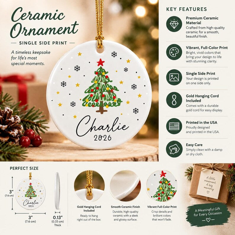 A round white ceramic ornament featuring a hand-drawn style Christmas tree with red and yellow ornaments, a red star topper, and black snowflakes. The name Charlie and the year 2026 are printed below.