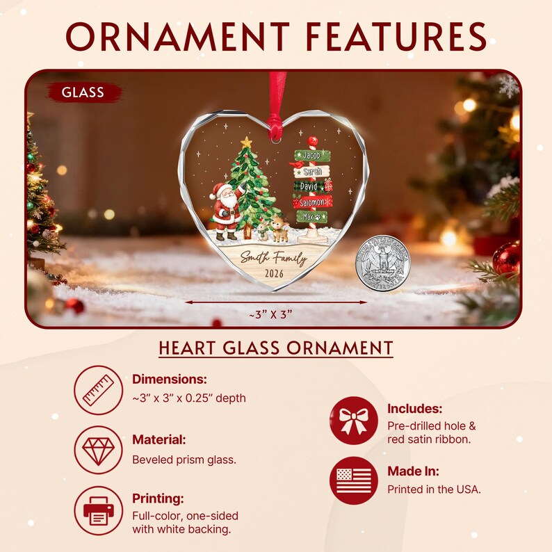 A heart-shaped beveled prism glass ornament featuring a printed illustration of Santa Claus, a Christmas tree, and a signpost with names. It includes a red satin ribbon and measures approximately 3 inches by 3 inches.