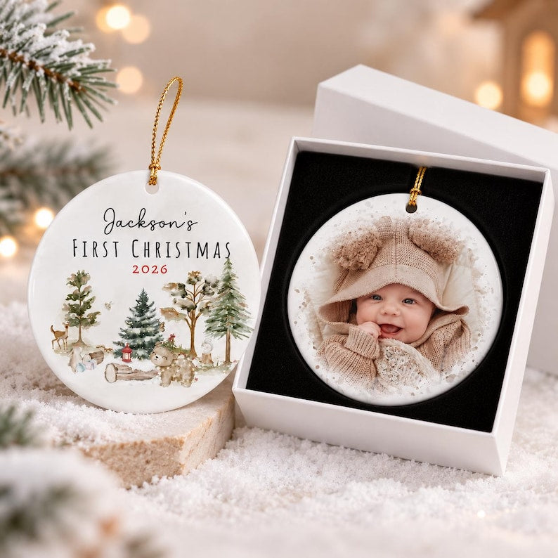 Two round white ceramic ornaments with gold hanging strings. One ornament features a watercolor forest scene with the text Jackson's First Christmas 2026.