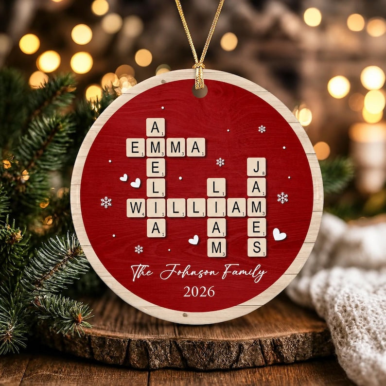 A round, red, wood-textured Christmas ornament featuring a crossword-style arrangement of letter tiles spelling the names Emma, Amelia, William, Liam, and James. The text The Johnson Family and 2026 are printed below the tiles.